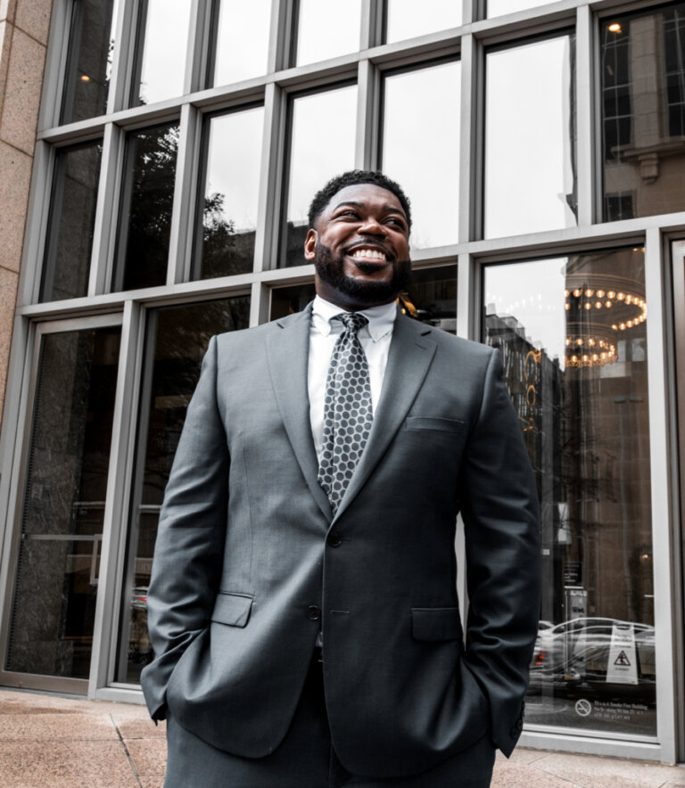 Attorney Joshua Palmer smiles confidently in a suit outside a modern office building