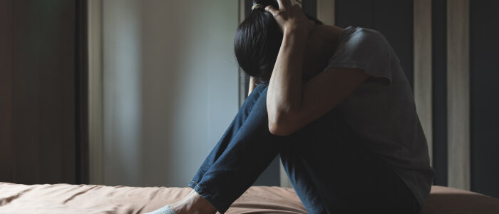A girl is hunched over on a bed in pain