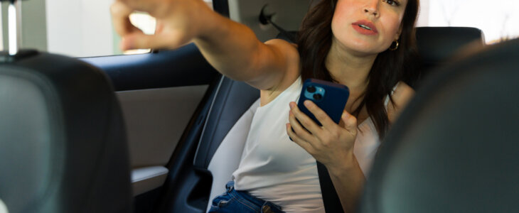Young woman using her smartphone to navigate or request a stop while enjoying a ride in a modern car sharing service