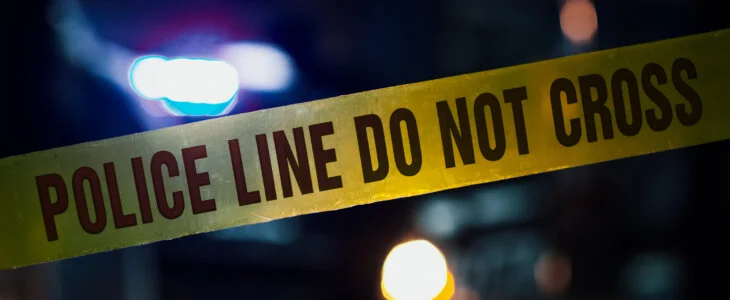 Close Up Shot Focused on Yellow Tape Showing Text Police Line Do Not Cross. Tape Used to Restrict a Crime Scene. Bokeh Background with Flickering Blue Siren Lights