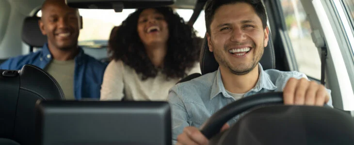 Happy Latin American crowdsourced taxi driver driving a couple and laughing in the car - mobility as a service concepts